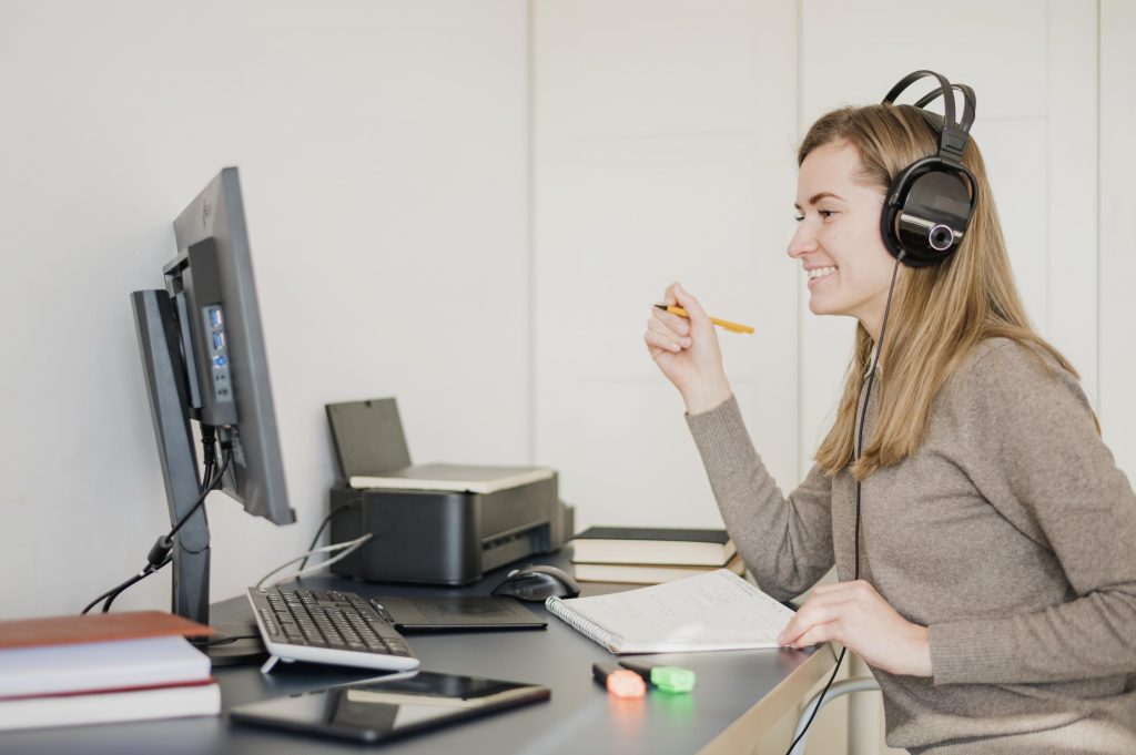 Frau sitzt vor einem Rechner und schreibt etwas auf einen Block. copyright: Freepik Company S.L. - www.freepik.com